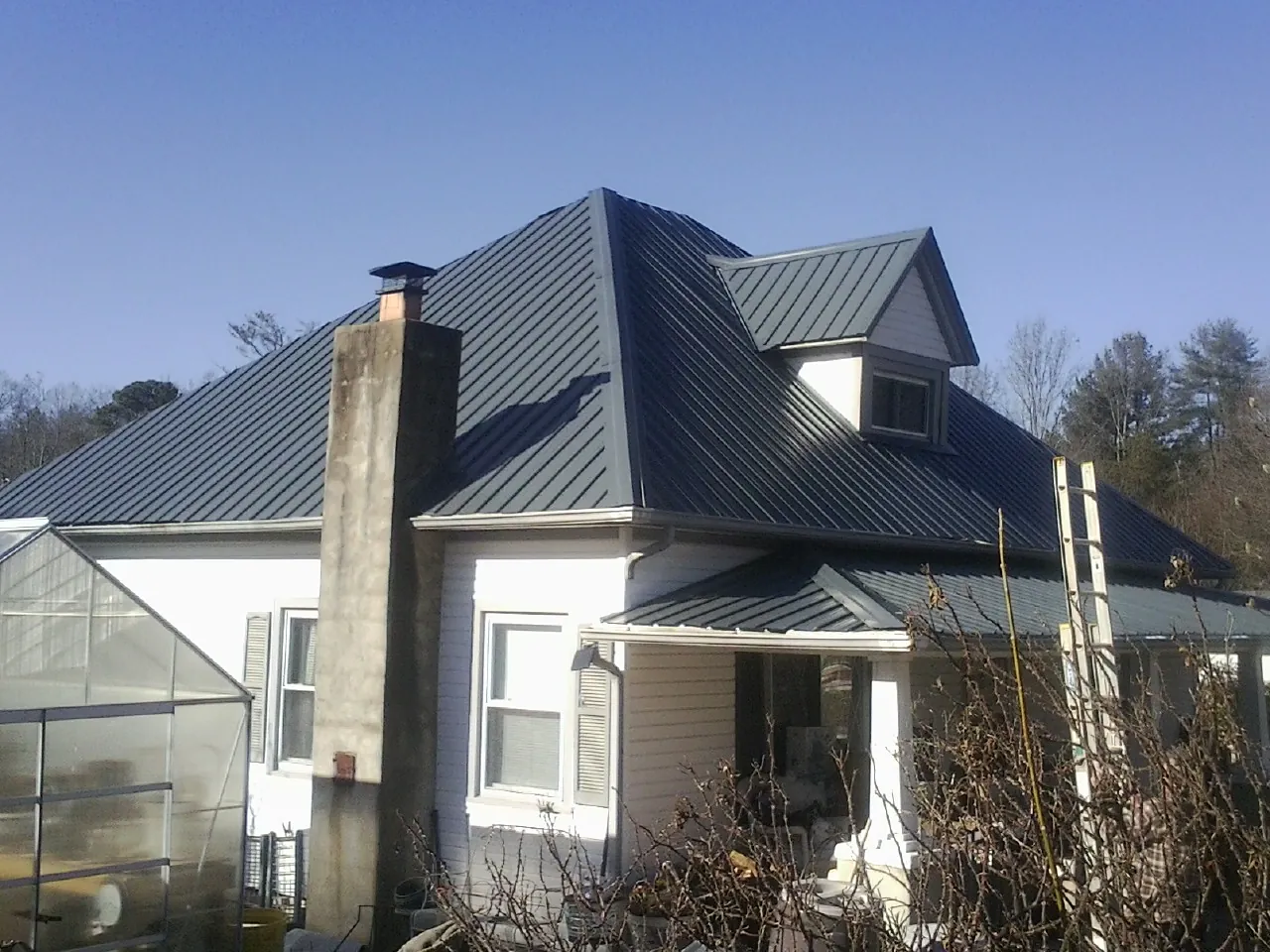 Dark blue standing seam metal roof on a white farmhouse with dormer — Slate & Tile Roof Repair by Roofing Brothers in Furlong