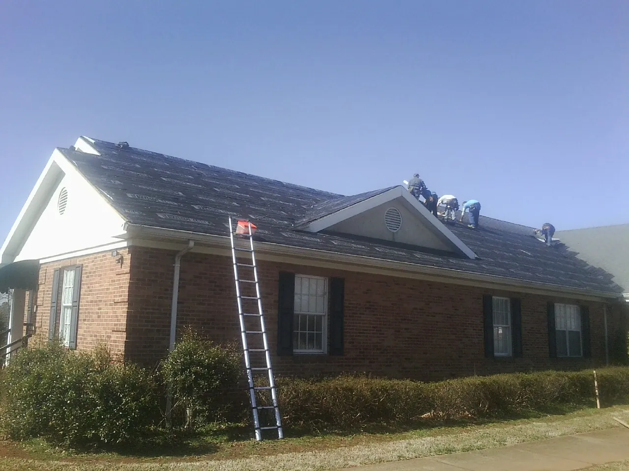 Crew tearing shingles off a brick ranch roof with a ladder set — Metal Roof Repair work by our crew in Furlong