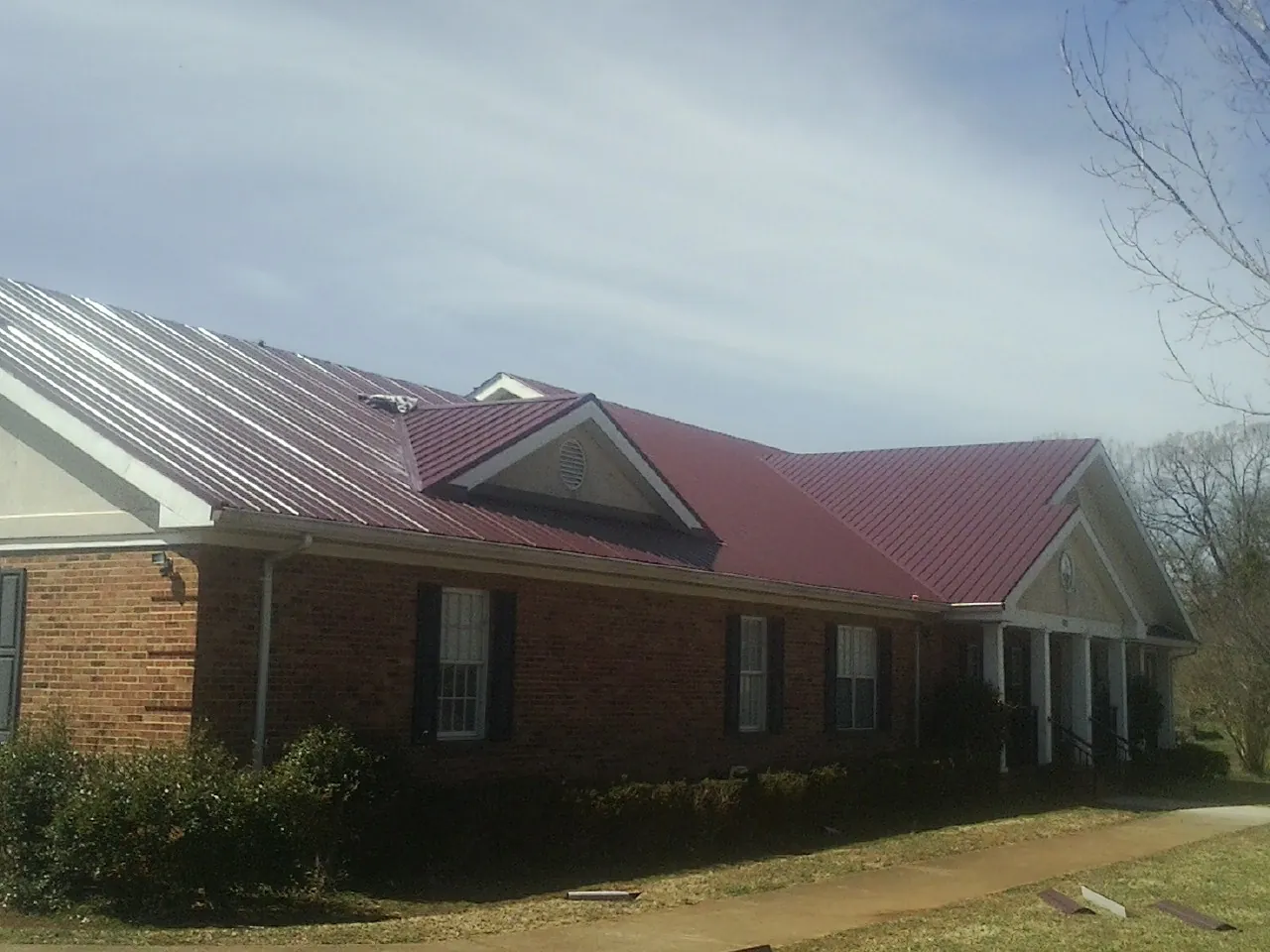 Red metal roof with gabled entries on a long brick building, from a Hail Damage Roof Repair job in Furlong