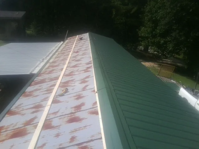 Old rusted panels beside newly installed green metal roofing — Wind Damage Roof Repair by Roofing Brothers in Furlong