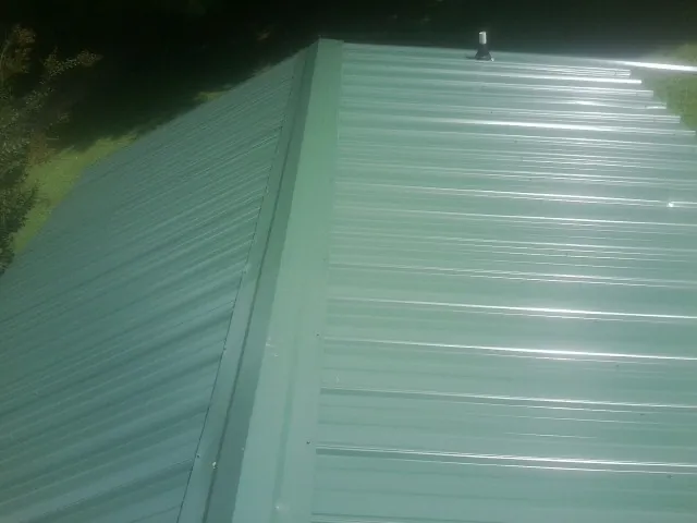 New green metal panels meeting at the ridge of a roof — Flat Roof Repair work by our crew in Furlong