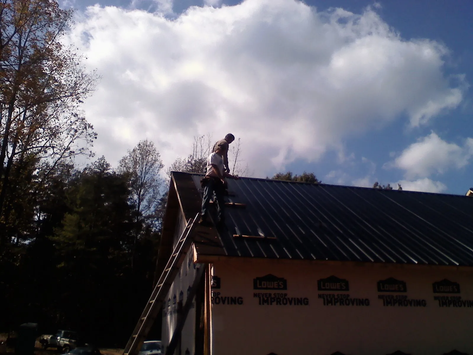 Roofer fastening dark metal panels high against a cloudy sky, from a Roof Inspection job in Furlong