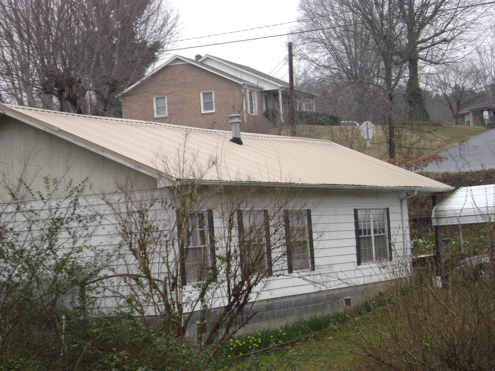 Tan metal roof on a white sided house set into a hillside — Commercial Roofing by Roofing Brothers in Furlong